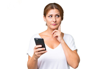 Middle-aged caucasian woman over isolated background using mobile phone and thinking