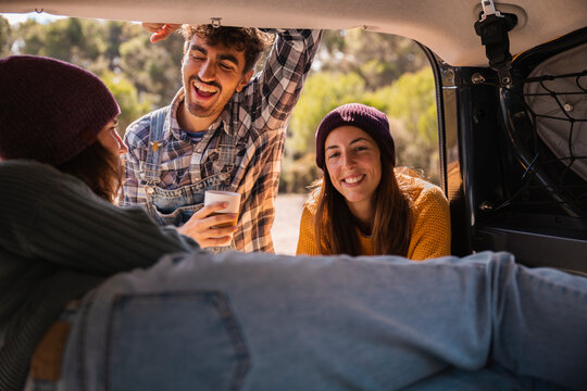Happy friends taking to woman in trunk of campervan