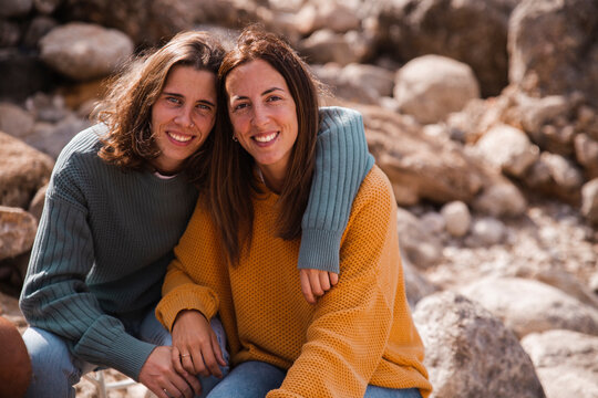 Smiling woman with arm around friend sitting on rocks
