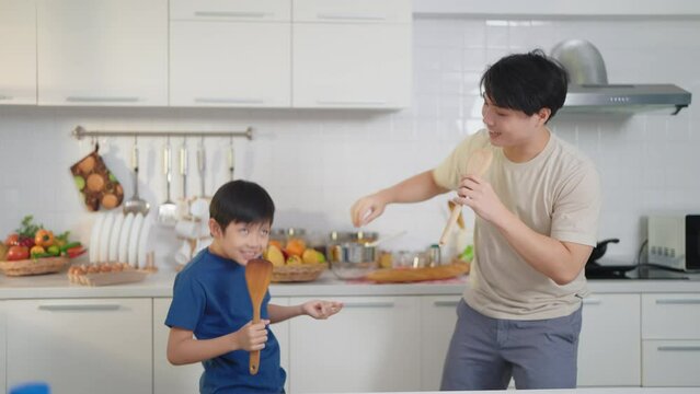 Asian father and son dancing happily in the kitchen at home while cooking. Single father concept