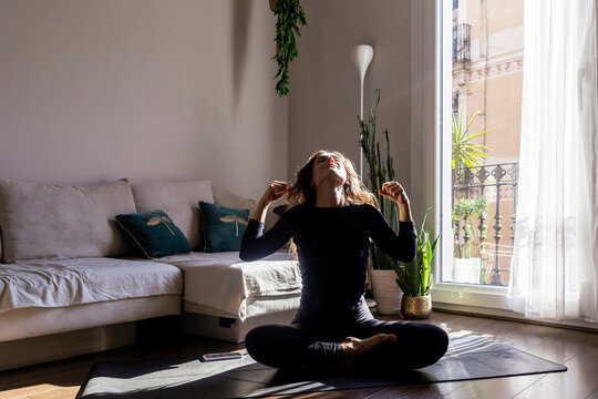 Woman doing yoga sitting on mat in living room at home