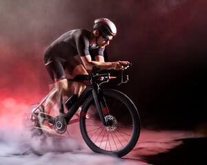 Sportsman sitting on turbo trainer against black background