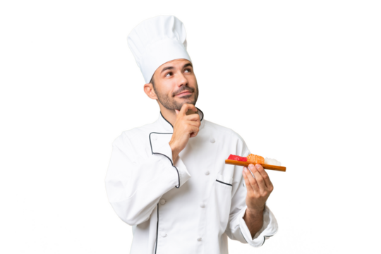 Young caucasian chef holding a sushi over isolated background and looking up