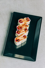Sweet sushi rolls with cherry and caramel on black plate