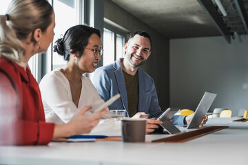 Smiling businessman with laptop sitting with colleagues at office