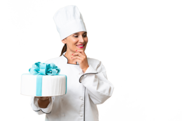 Middle-aged chef caucasian woman with a big cake over isolated background thinking an idea and looking side