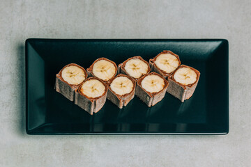 Sweet sushi rolls with banana and chocolate on black plate