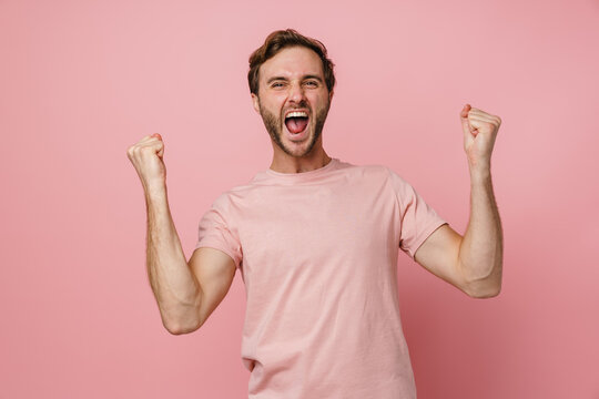 Young man smiling and clenching fists like winner isolated over pink wall