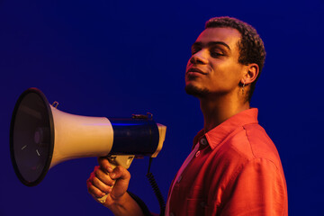 African man holding megaphone while standing isolated over blue background