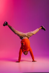 African man doing handstand while dancing isolated over over pink neon studio background