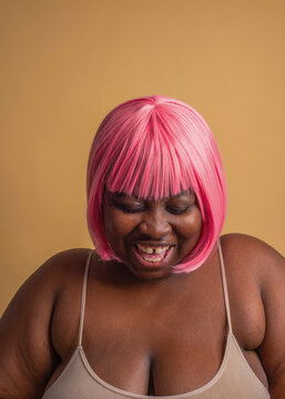 Cheerful plus size woman wearing pink bob wig against beige background