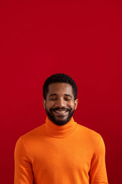Smiling young man with eyes closed against red background