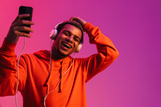 African man listening music with headphones and mobile phone isolated over pink background