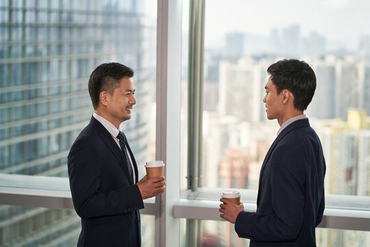 two asian business men standing and talking by the window in office