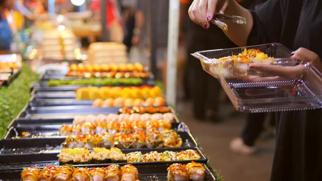 Local Asian Street Food: Woman Choosing Traditional Japanese Sushi and Rolls at Night Market. High Quality 4K Slow Motion Cinematic Foodie Concept Footage. Bangkok, Thailand.