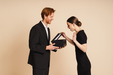 Man giving gift box to his surprised girlfriend isolated over beige wall