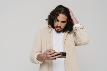 Upset hispanic man playing online game on mobile phone isolated over white wall