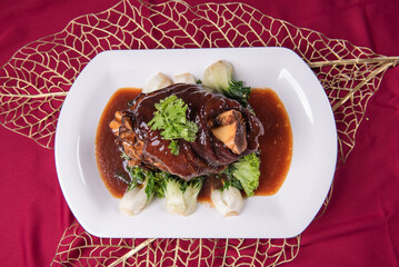 stewed pork trotters whole leg in brown red wine sauce with green vegetables on red cloth background asian chinese western banquet meat menu for restaurant fine dining hotel