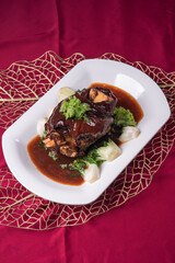stewed pork trotters whole leg in brown red wine sauce with green vegetables on red cloth background asian chinese western banquet meat menu for restaurant fine dining hotel