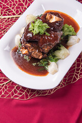 stewed pork trotters whole leg in brown red wine sauce with green vegetables on red cloth background asian chinese western banquet meat menu for restaurant fine dining hotel