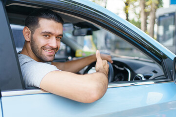 Happy cheerful Asian ale car driver waving or showing thumb up and smiling out of the car. Happy...