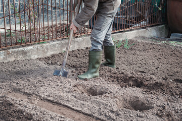 A man in boots is working in the garden, digging black soil. A worker with a shovel digs a bed...