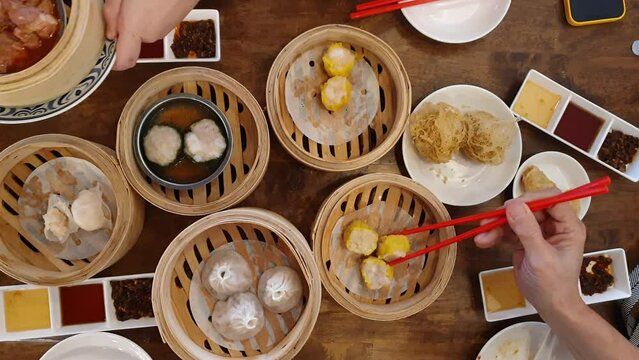 Hands chopsticks eating dim sum shu mai Chinese hong kong style breakfast food steamed dumplings stuffed meat