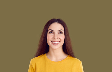 Attractive cute brown-haired Caucasian woman looks up with smile at free space for your promotional offer or text and dreams of new shopping wearing yellow t-shirt, stands on brown background