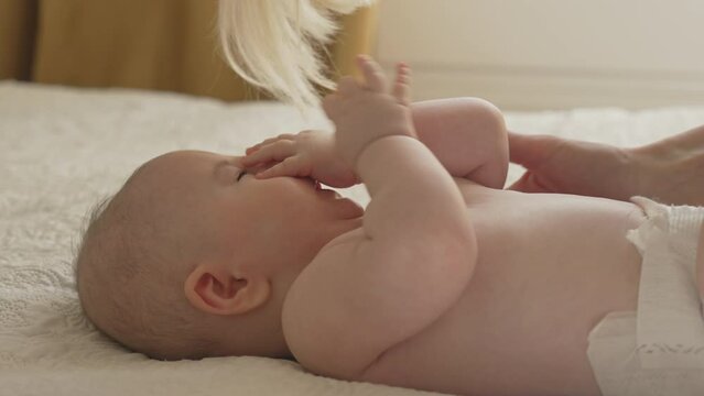 Tired Baby lied in bed by his mothers hands, grumpy little hands covering his face