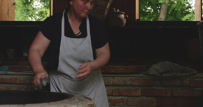 Woman In Apron Pours Out Ashes On Traditional Tone Oven. - close up