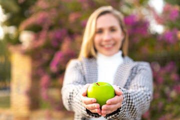 Young blonde woman with an apple at outdoors