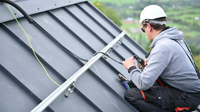 Man worker prepearing for mounting photovoltaic solar modules on roof of house. Electrician in helmet installing solar panel system outdoors. Concept of alternative and renewable energy.