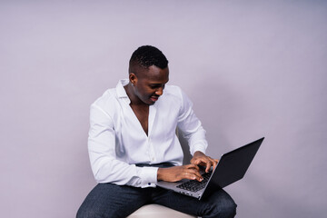 Optimistic african-american male student in casual shirt using laptop pc isolated
