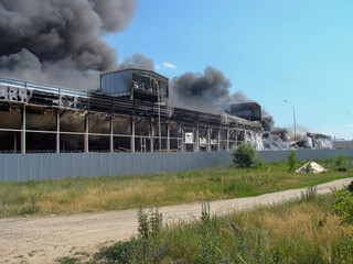 Fototapeta na wymiar Warehouse fire with black thick smoke against a clear sky. Sandwich panels are burning