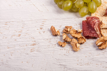 Ham, nuts, crackers and grape on white wooden vintage background in studio photo