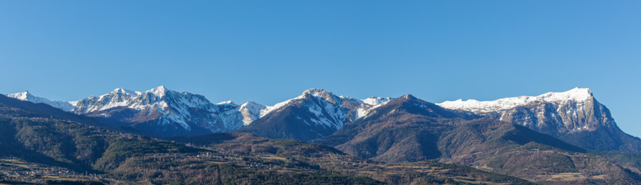 A scenic panoramic view of majestic snowy mountain range with pine forest under a majestic blue sky