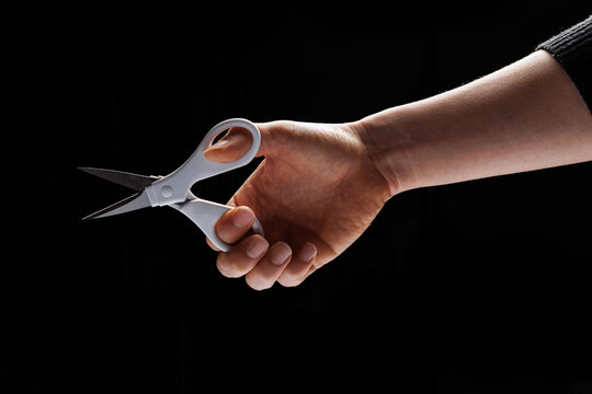 On a black background, a man is holding scissors with his hand