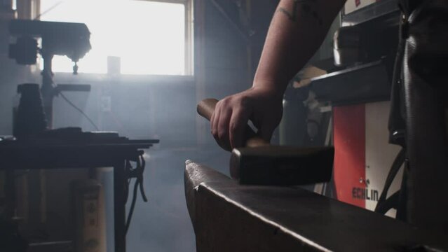 A blacksmith puts down a hammer after shaping a piece of metal on an anvil