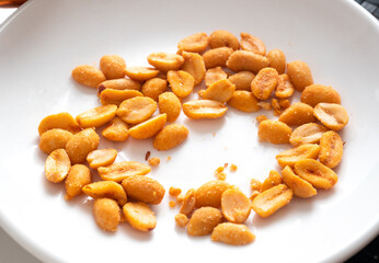 Pile of peanuts with salt and spices on white plate. Tasty snack.