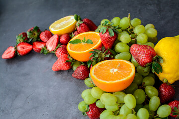Various fruits and berries on dark gray background in the kitchen