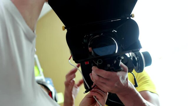 Cameraman operator holds cinema camera in hands, lens with matte box. Backstage filming of movie indoors. Cinematography. Production of commercial ad or TV series. DOP is on set scene. Videography