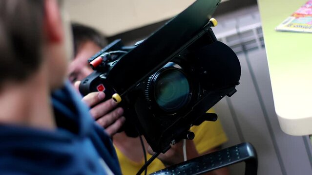Cameraman operator holds cinema camera in his hands and shoots scene, backstage filming movie indoors. Cinematography. Production of commercial ad TV series. Lens with matte box. Handheld videography