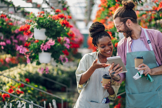 Multiracial couple of gardeners working in a greenhouse while drinking coffee and using tablet - Powered by Adobe