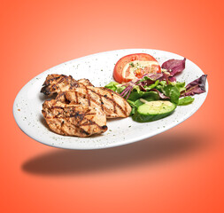 Floating  White plate with roasted chicken fillet and salad