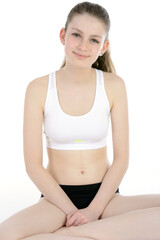 Athletic teenage girl in sportswear is sitting in studio, isolated on white