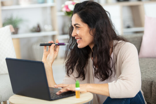 mature woman working on laptop and smoking an electronic cigarette