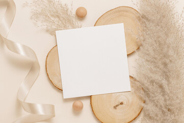 Paper sheet mockup card on wooden stand with pampas grass and ribbon, neutral beige background. Minimal aesthetic background card for wedding, greeting and invitation, logo and design. Top view