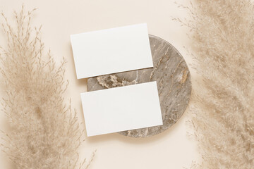 Two blank paper sheet mockup cards on marble stand with pampas grass, flat lay, top view. Minimal aesthetic business card with copy space for greeting, branding, logo and invitation