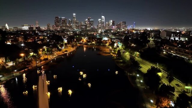 Aerial view flying over Los Angeles Echo park illuminated lake fountain towards futuristic city skyline