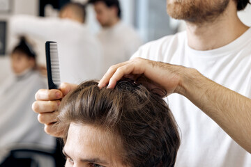 close-up, professional male hairstylist combing young customer's hair